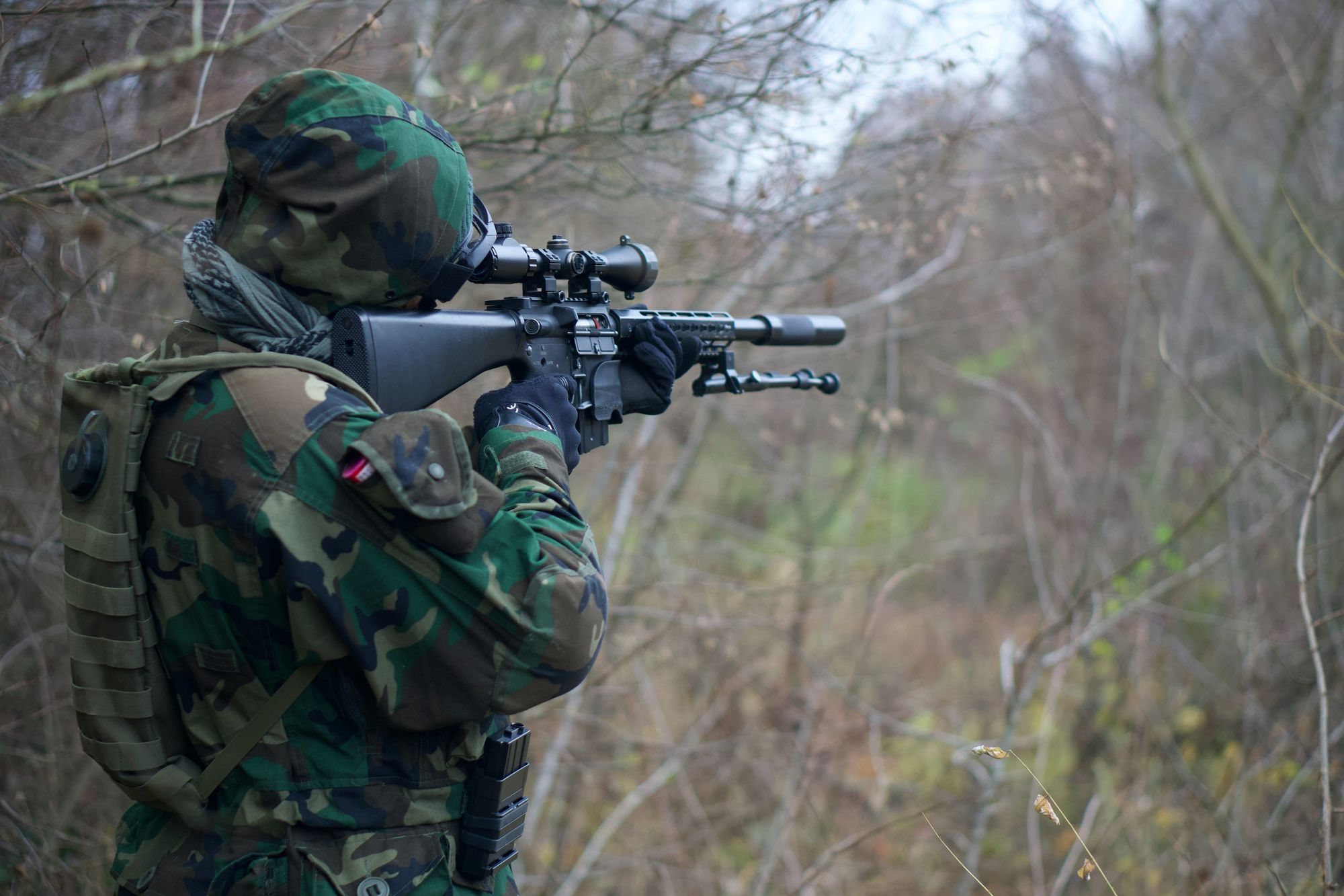 Camouflage soldier with rifle and scope, aiming at a target.